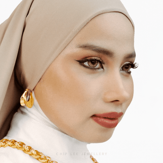 Woman wearing a beige hijab and gold jewelry on a white background