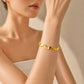 A close-up of a model's wrist wearing a gold wavy cuff bracelet with textured and polished segments, set against a soft beige background.